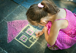 Girl drawing house with chalk on sidewalk