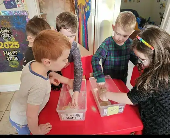 Children touching salt and sand inside trays
