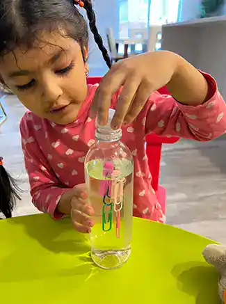 child putting paper clips in bottle of water